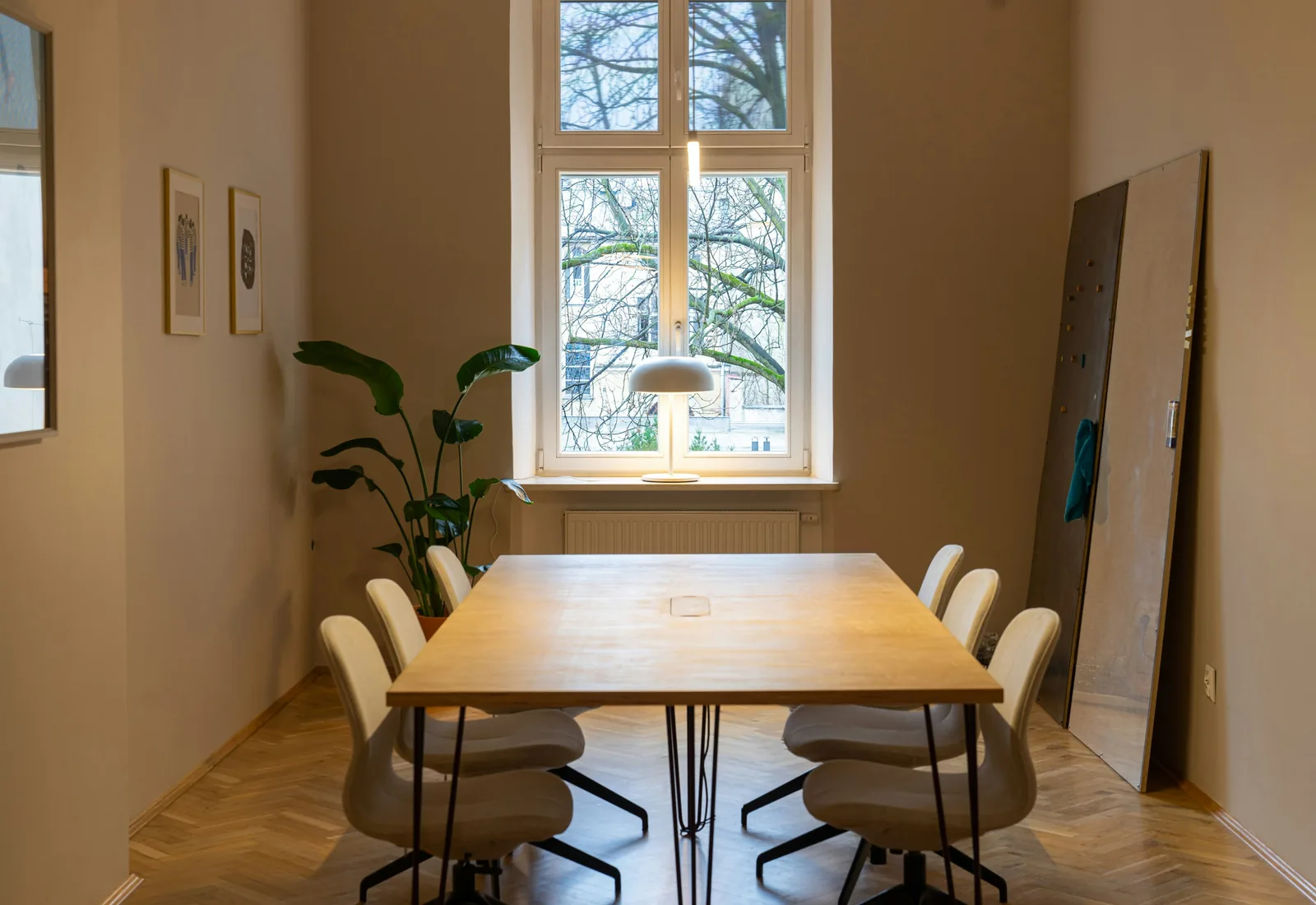 A small meeting room with a wooden table, six chairs and a tall window